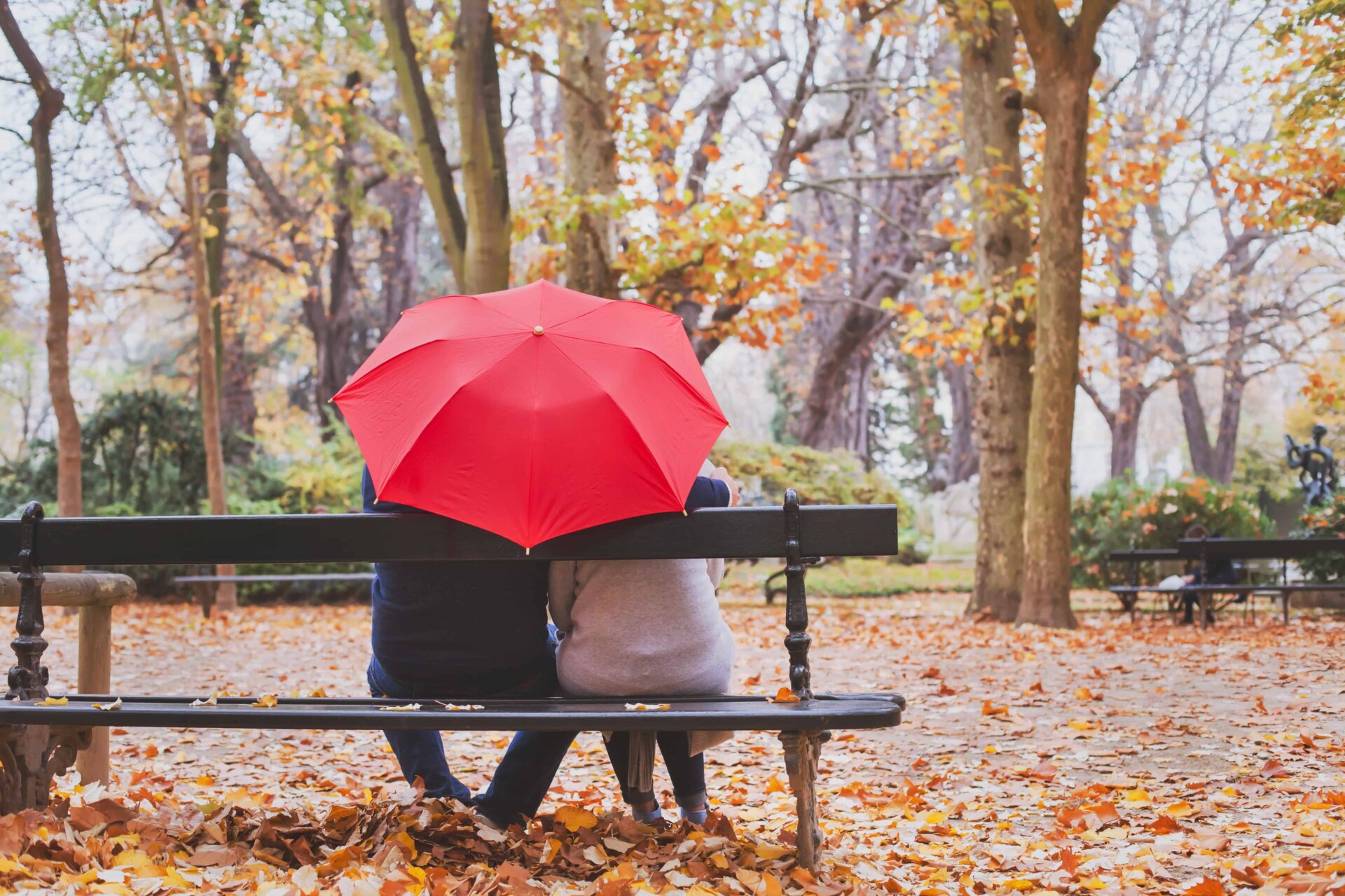 couple sat on outdoors underneath coloured red umbrella