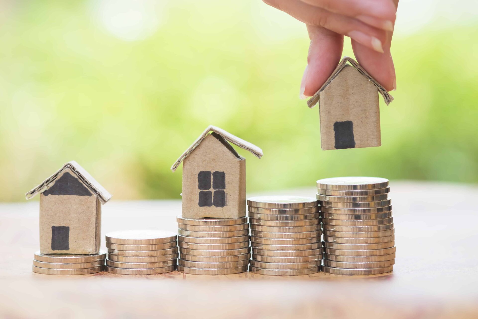 person stacking paper houses on top of piles of money