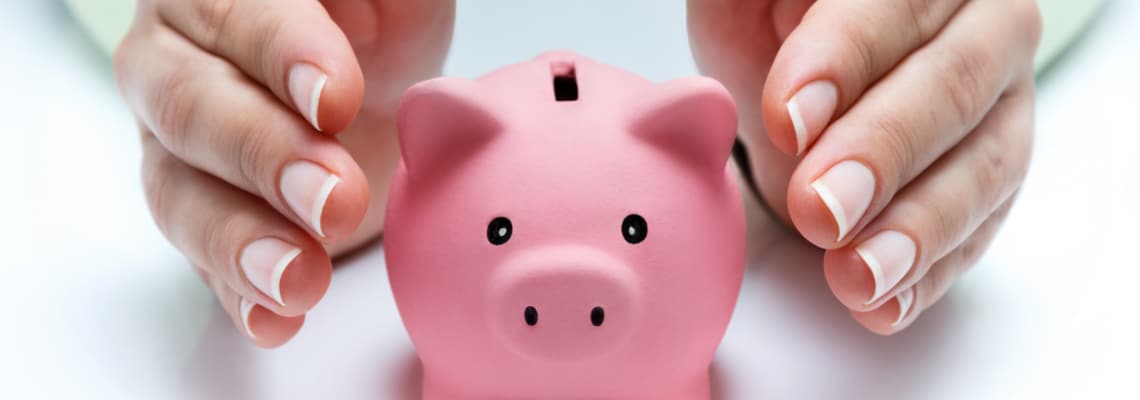 piggy bank being shielded by persons hands
